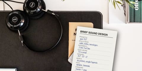 A handwritten sound design brief on a desk, next to studio headphones and a notebook