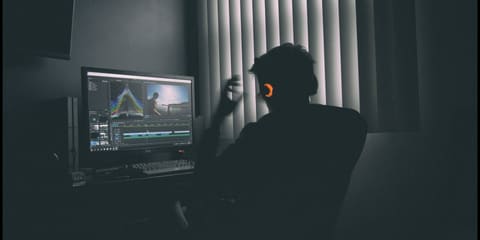 Un homme au casque travaille à l'ordinateur dans un studio sombre, avec le montage de la vidéo à l'écran