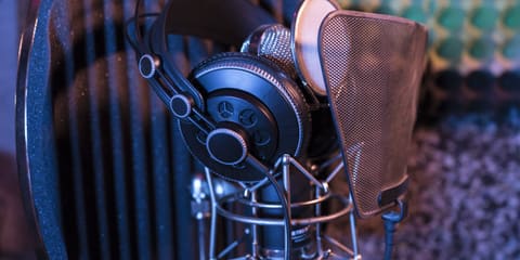 Cuffie appoggiate su un microfono da studio con filtro anti-pop, davanti a un pannello fonoassorbente